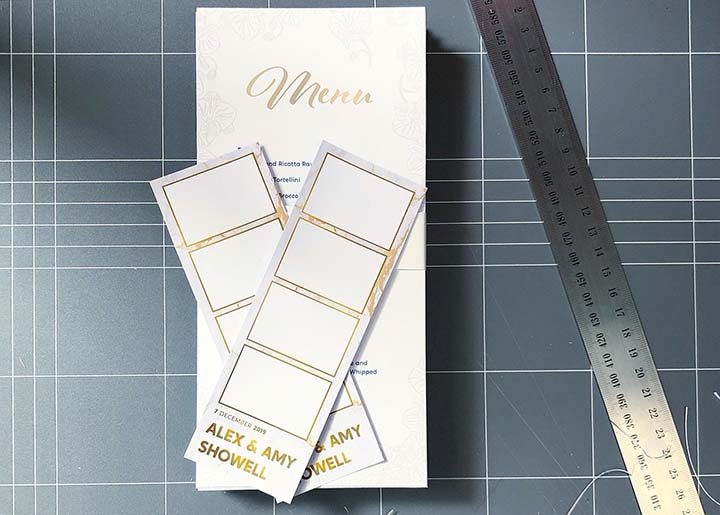 Photobooth strips on top of a wedding menu, with a ruler and cutting mat in the background.